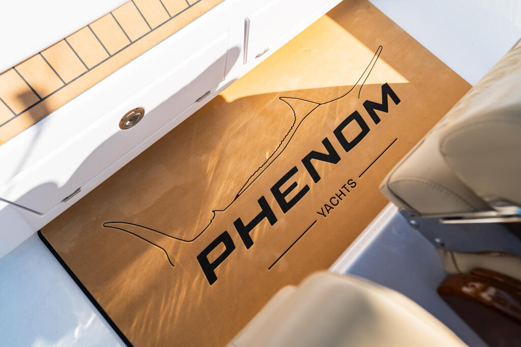 Phenom Yachts logo on wooden helm pad with white boat hardware and cushioned seating visible