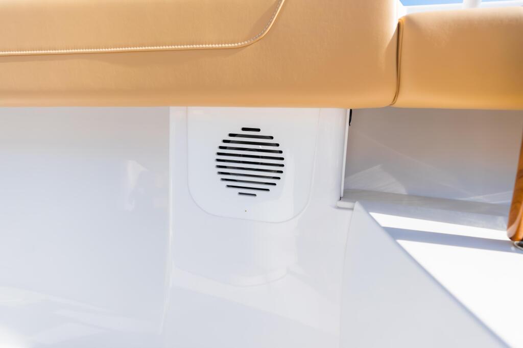 Cabin speaker grille mounted on white wall below tan upholstered seating