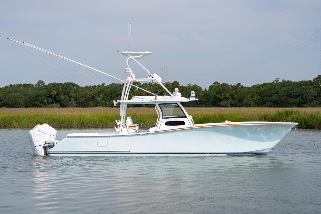 White center console fishing boat with tall tower and outboard motor docked in shallow saltwater near marsh grass