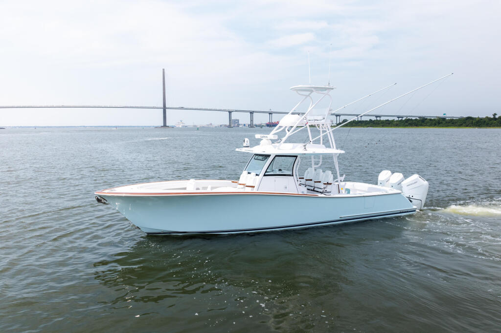 Light blue center console fishing boat with tower anchored in shallow water near a suspension bridge