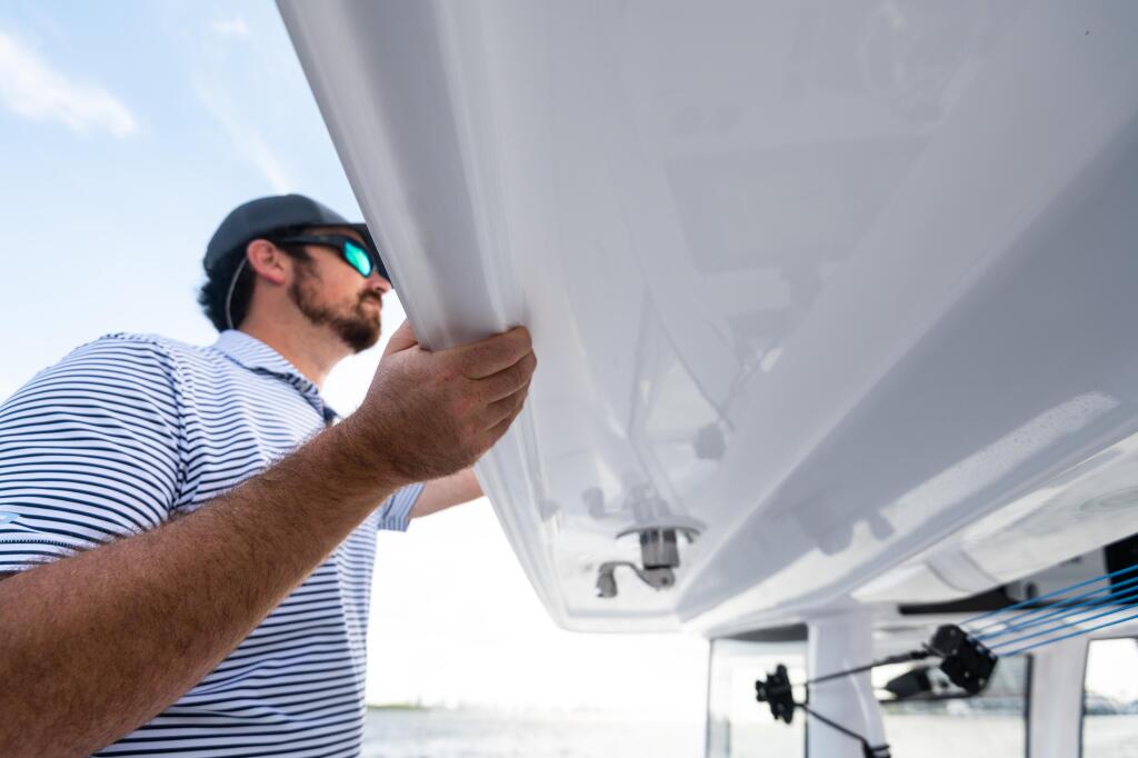 Man in striped shirt and sunglasses inspecting the underside of a boat's hard-top canopy