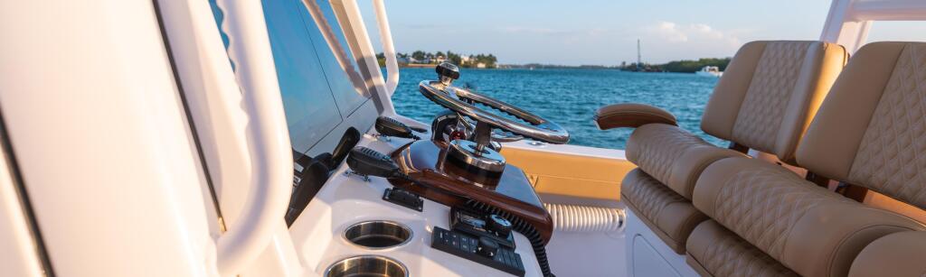 Helm of a boat with brown quilted seating, steering wheel, and controls overlooking open water at golden hour