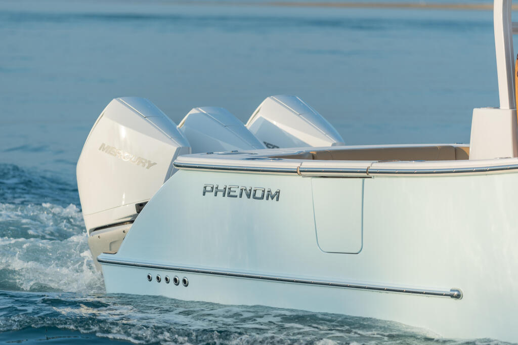 White Phenom boat with triple Mercury outboard engines anchored in shallow turquoise water near shore