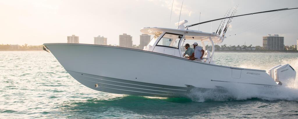 White center console fishing boat with fishing rods running through shallow beach waters with coastal buildings in background