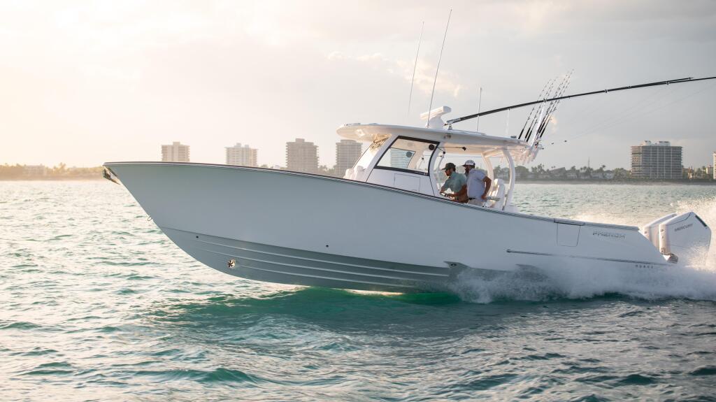 White center console fishing boat with fishing rods running through shallow beach waters with coastal buildings in background