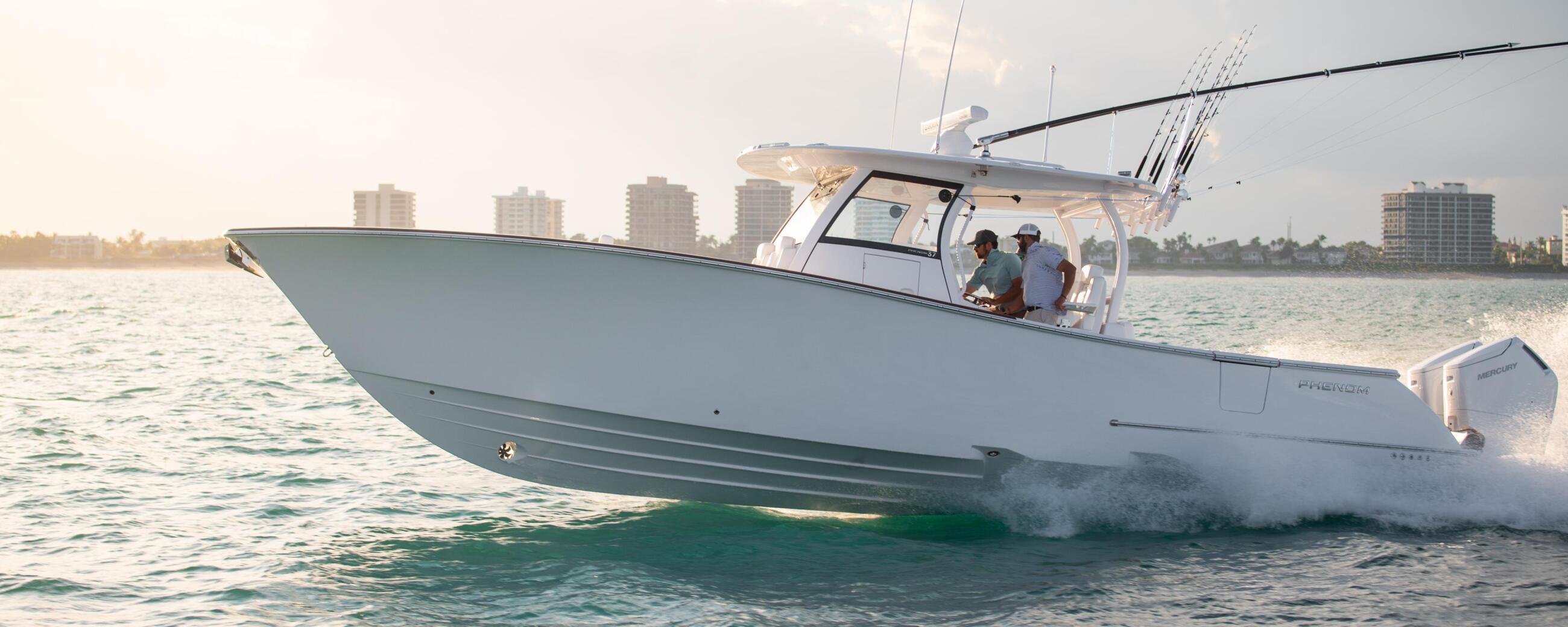 White center console fishing boat with fishing rods running through shallow beach waters with coastal buildings in background