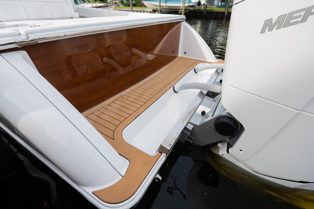 Transom seating area with faux teak flooring and white cushioned seats on a docked boat