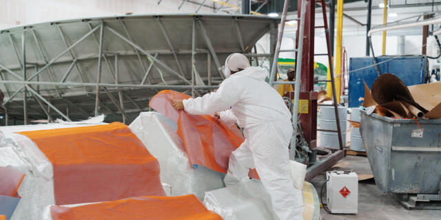 Worker in white protective suit handling orange and white boat cover material in manufacturing facility