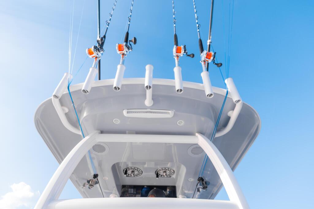 Multiple fishing rod holders with orange and white reels mounted on the hard-top of a sport fishing boat against blue sky