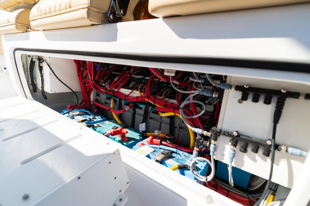 Open electrical compartment showing organized red wiring, battery banks, and blue fuses on a boat engine installation