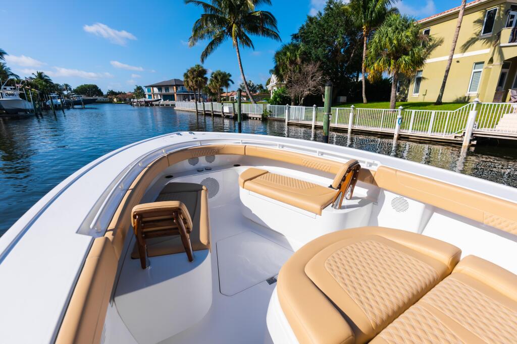 Spacious bow seating area with tan cushioned seats and removable backrests on a white center console boat docked at a tropical marina