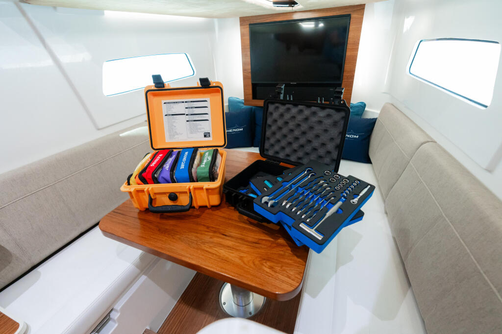 Boat cabin interior with tool kit and first aid supplies on wooden table between cream seating
