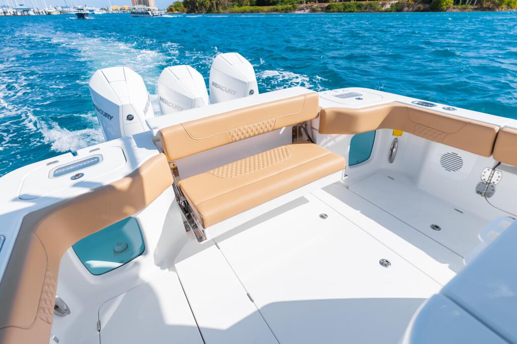 Spacious boat cockpit with tan and white seating, three Mercury engines, and moored boats visible in turquoise water