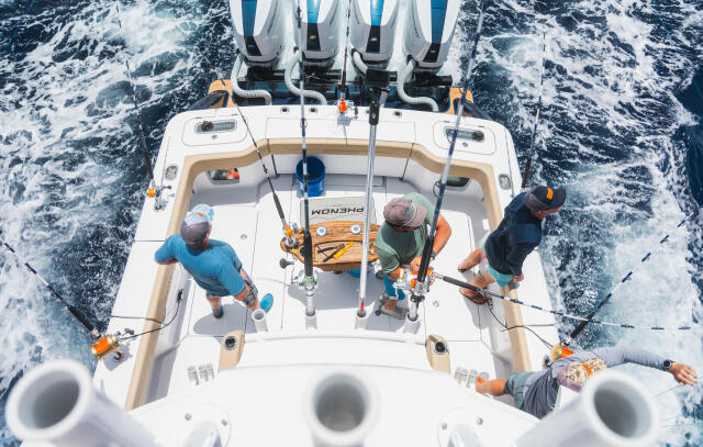 Aerial view of fishing boat with four anglers holding rods while cruising through offshore waters
