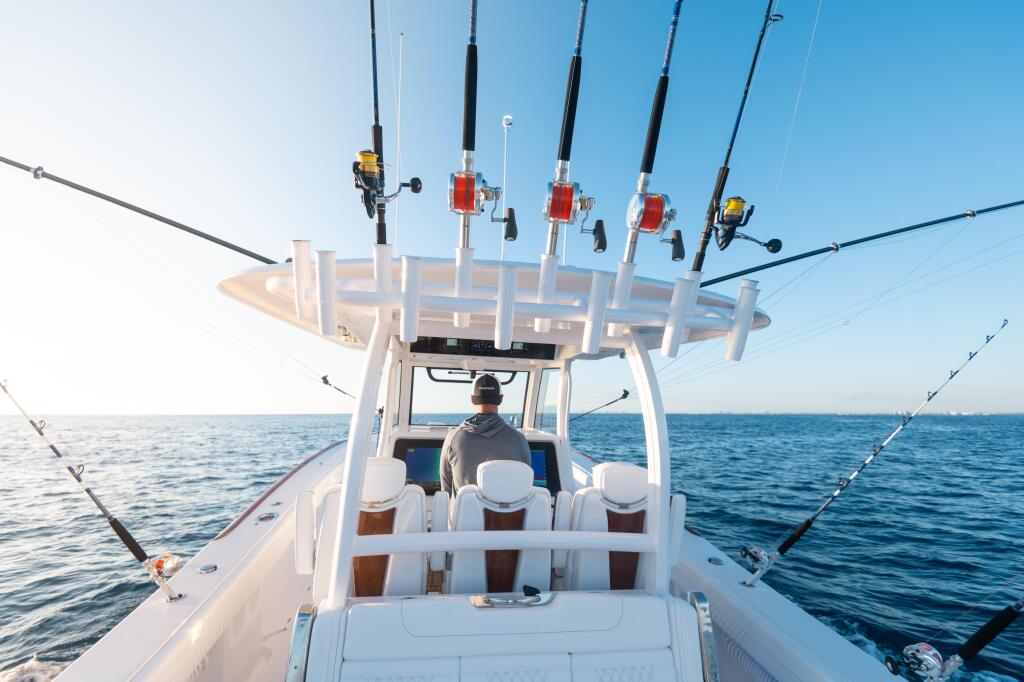Captain at helm of fishing boat with multiple rod holders mounted on hard-top canopy under clear blue sky