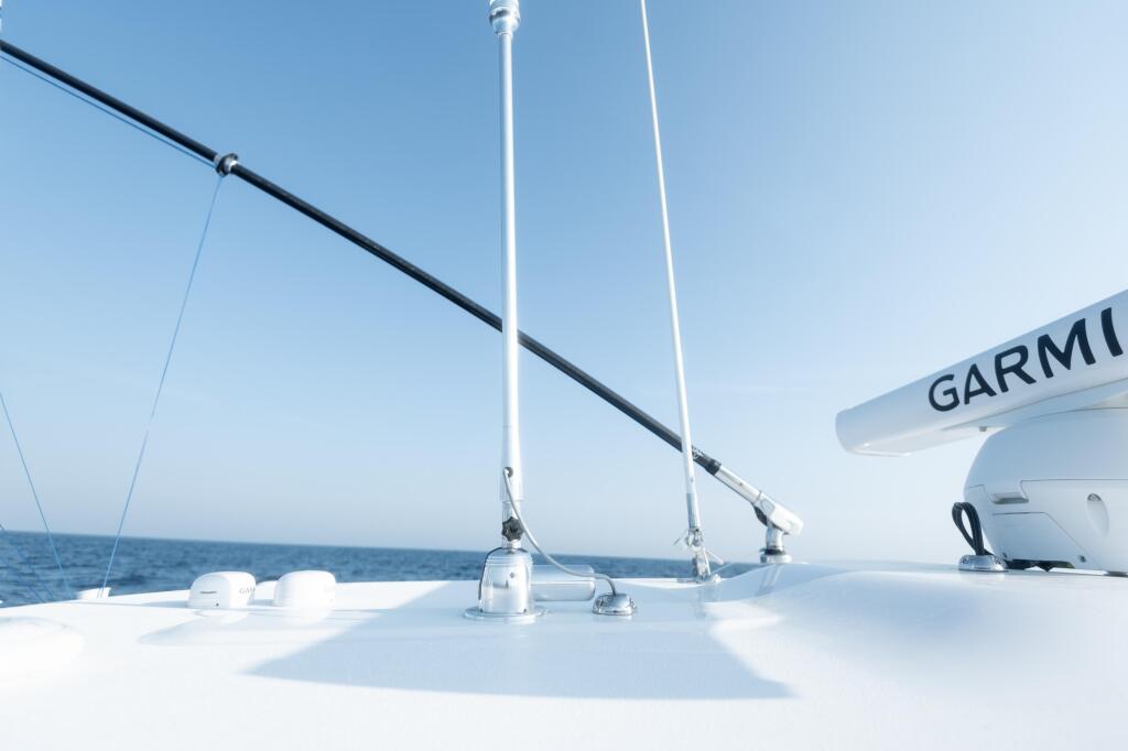 Boat deck with Garmin electronics mounted on white console, rigging and antenna visible against calm blue water