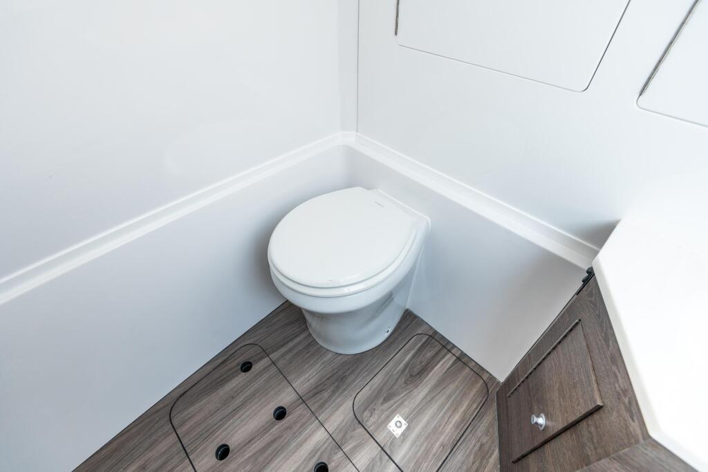 Compact marine toilet with white porcelain bowl and gray wood-grain flooring in a small cabin space