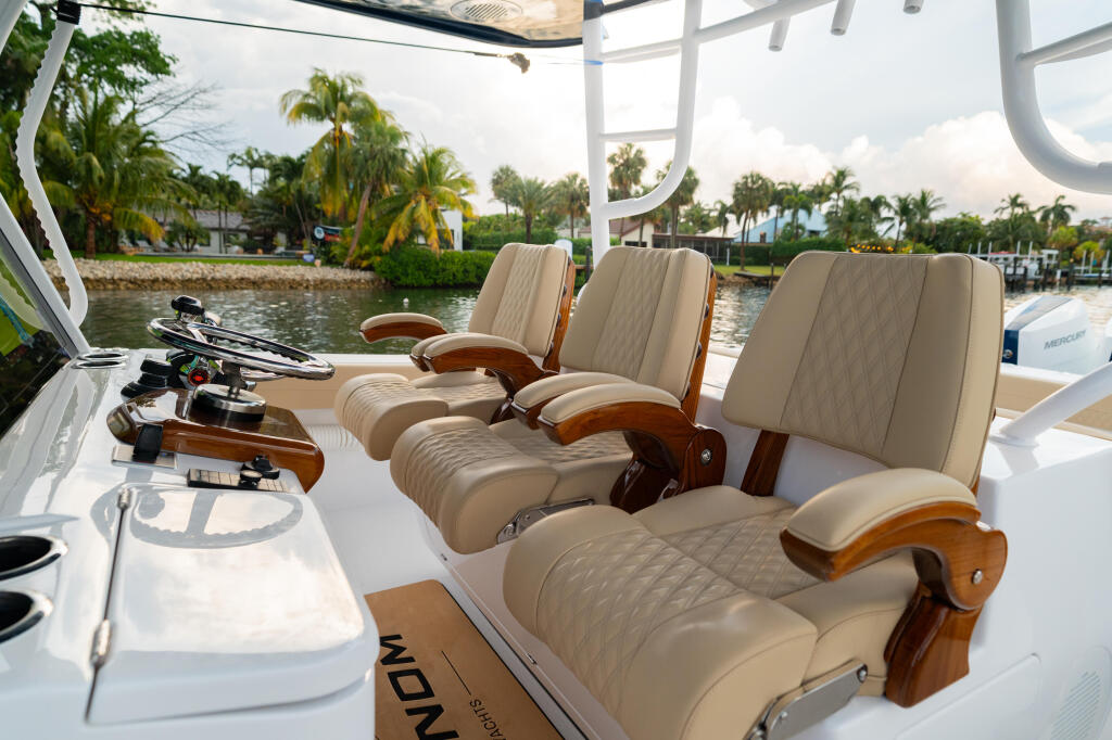 Helm seating with three premium captain's chairs under a hard-top, overlooking a marina with palm trees and docked boats