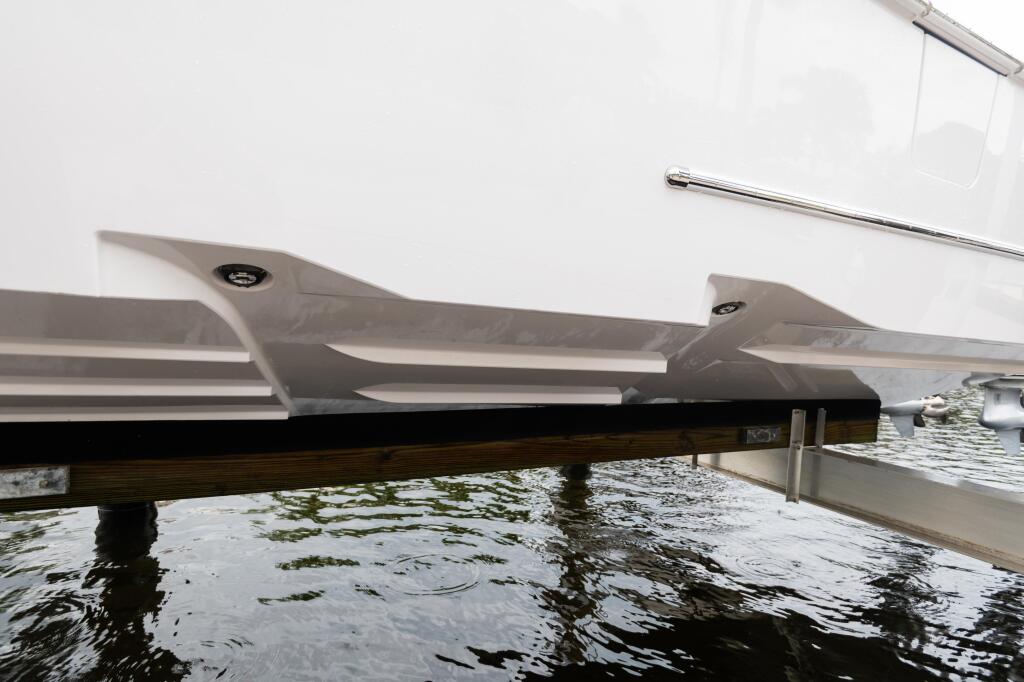 Boat hull detail showing white fiberglass construction and dark wooden dock structure at waterline