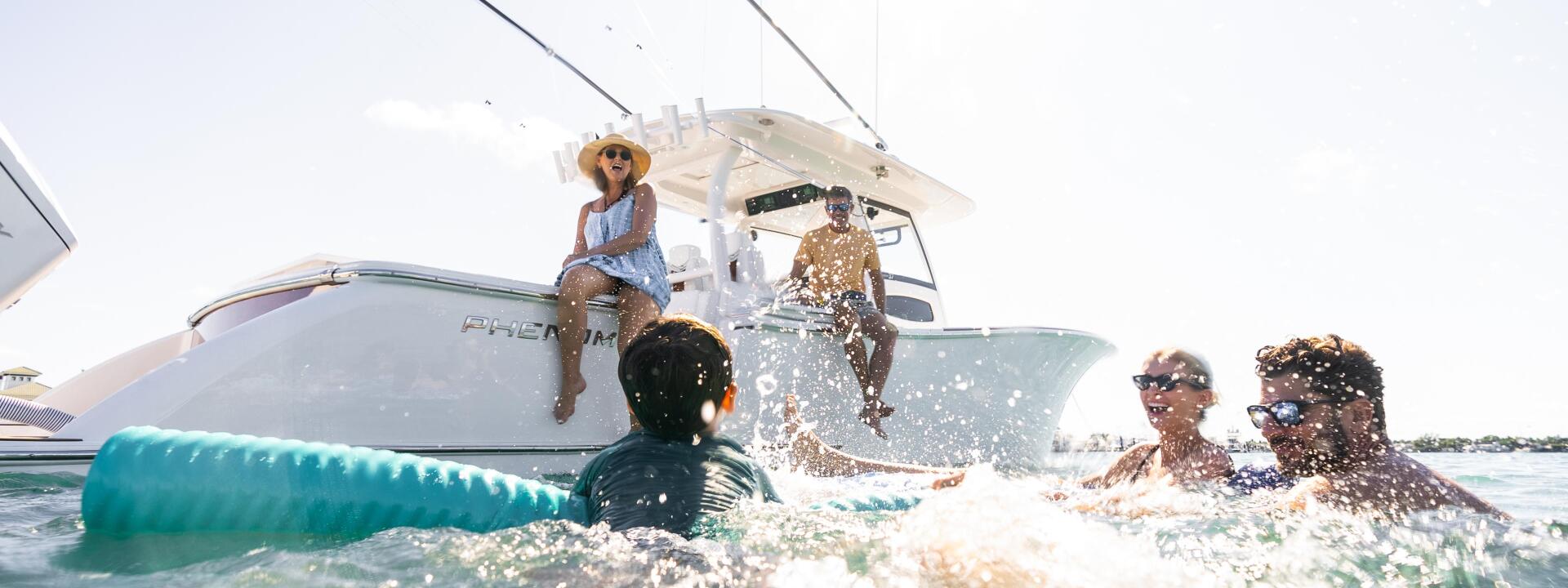 Family swimming and splashing in shallow water near a boat anchored at a sandbar