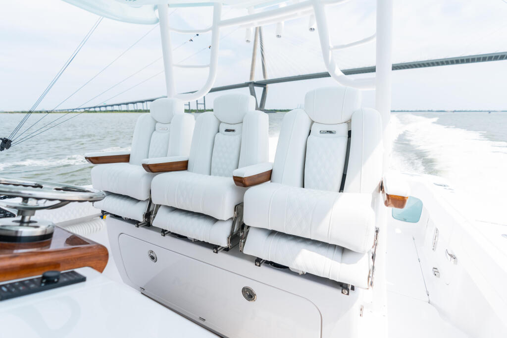 White cushioned seating with wood accents inside a boat cabin with hard-top and wide views of the water