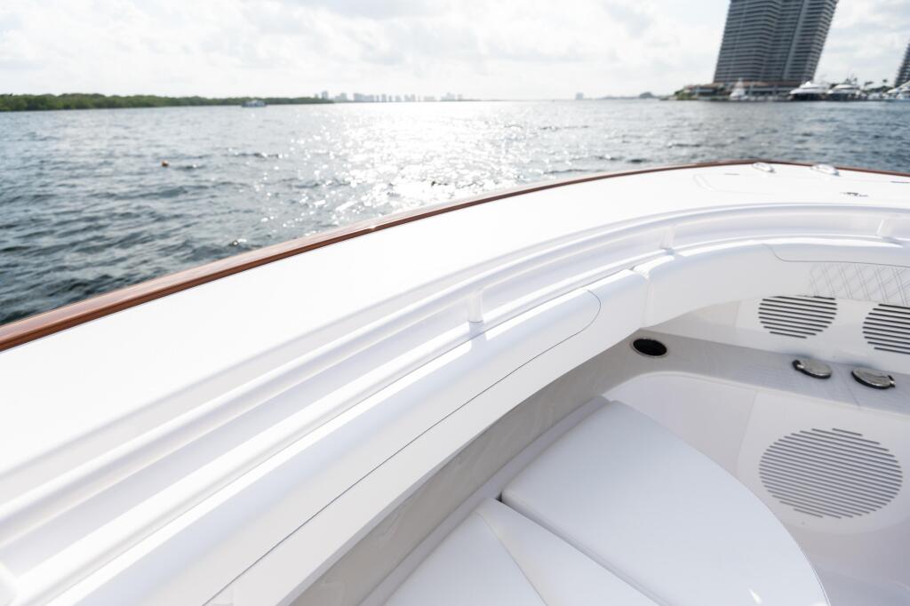 Bright white boat bow with curved handrails and ventilation details overlooking calm water and distant shoreline