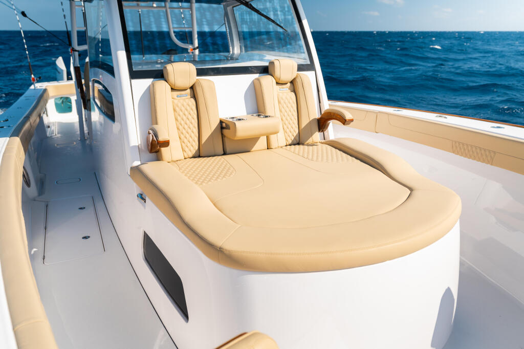 Cream-colored chaise lounge seating with armrests and captain's chairs on a white center console boat in open ocean