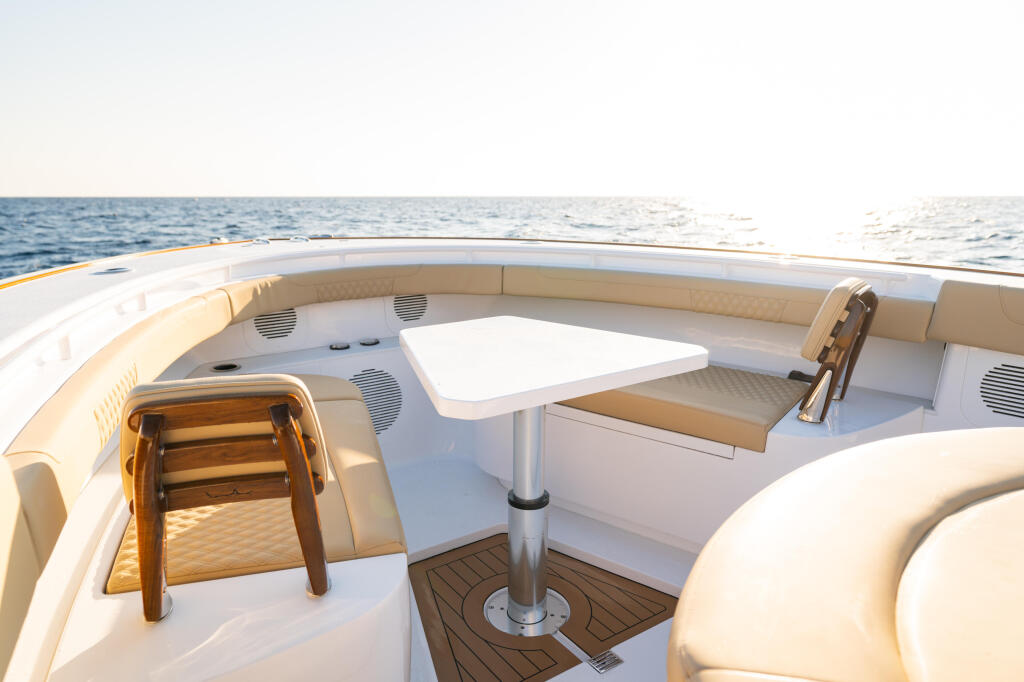 Spacious boat cockpit with cream seating, white dining table, and teak decking overlooking calm ocean waters