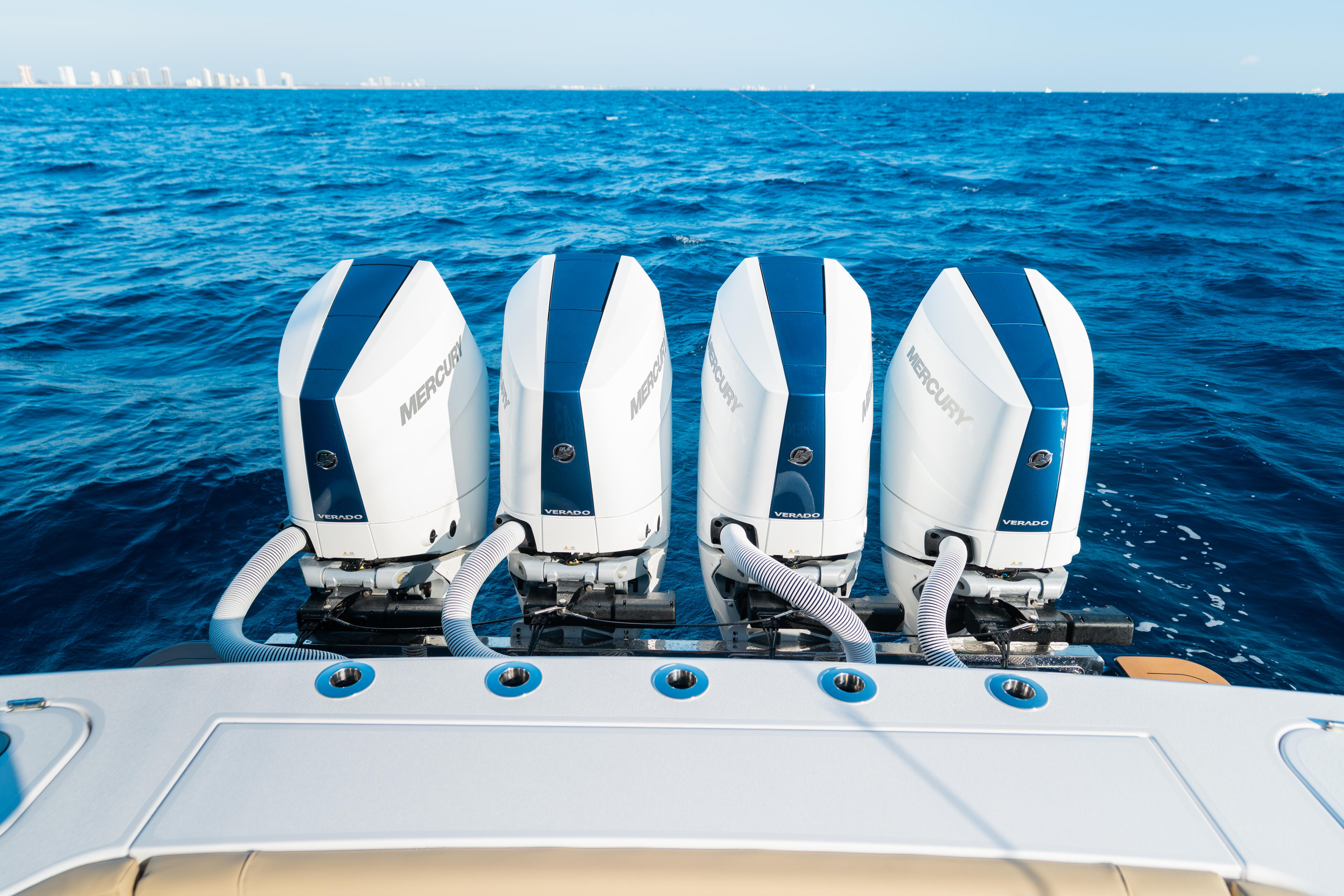 Four white and blue Mercury outboard engines mounted on the transom of a boat facing open ocean