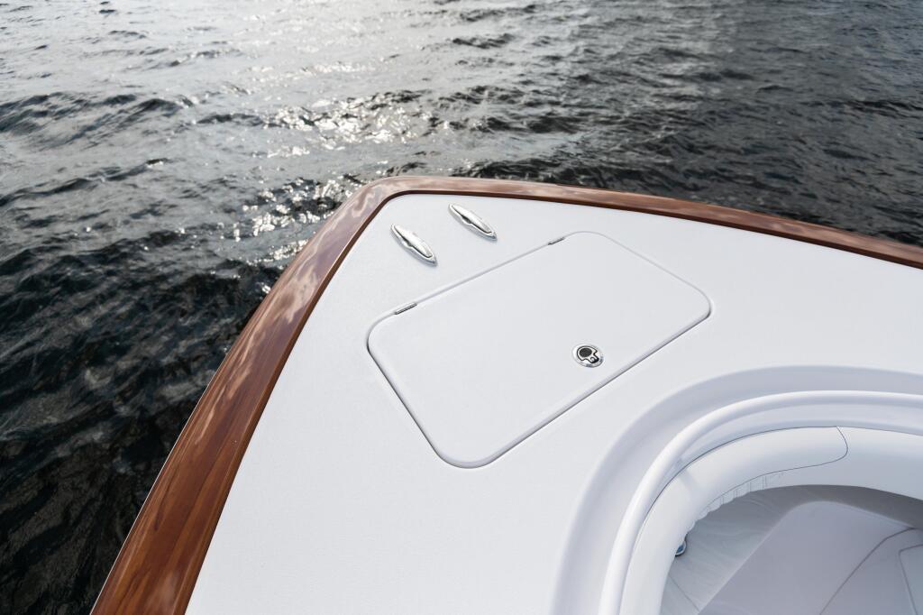 Boat's white bow deck with faux-teak rail and access hatch overlooking calm water