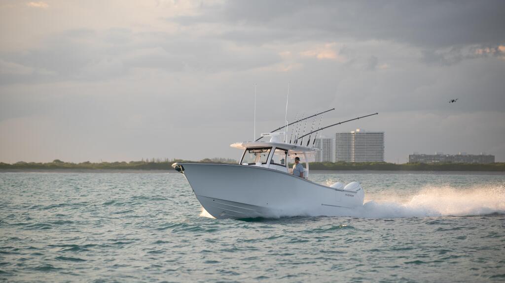 White sportfishing boat with tall antennas running through offshore waters near coastal high-rises